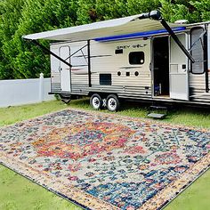 an rv is parked on the grass with a rug underneath it and trees in the background