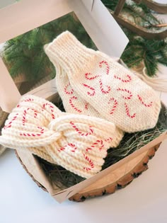 two knitted mittens sitting in a box on top of a wooden table next to a christmas tree