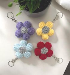 four crocheted flower keychains sitting on a white surface next to a potted plant