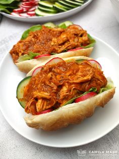 two sandwiches with meat and veggies on buns sitting on a white plate