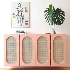 a pink cabinet with three doors and a potted plant in the corner next to it