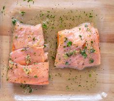 two raw salmon fillets on a cutting board with seasoning sprinkles