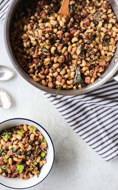 a pot filled with beans and greens on top of a striped towel next to spoons