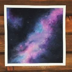 a painting of the night sky with purple and blue stars in it on a wooden surface