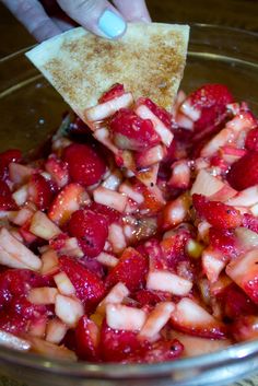 someone is dipping strawberries into a bowl with tortilla chips on the side