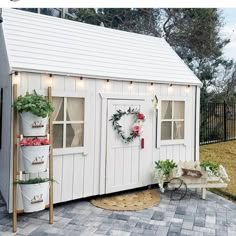 a small white shed with potted plants and wreaths on the front door area