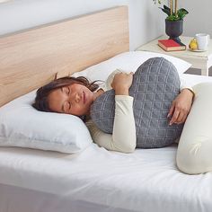 a woman laying on top of a white bed next to a wooden headboard and night stand