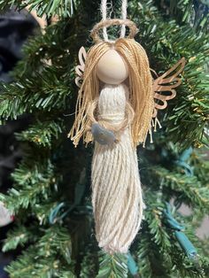 an angel ornament hanging from a christmas tree with pine needles and twine