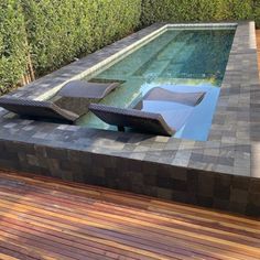 an empty swimming pool with two lounge chairs on the edge and wood decking around it