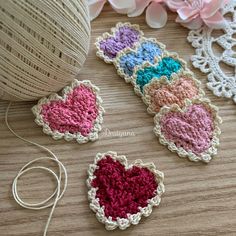 three crocheted hearts sitting on top of a table next to a ball of yarn