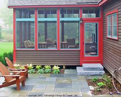 a red house with two wooden chairs in front of it and an enclosed patio area