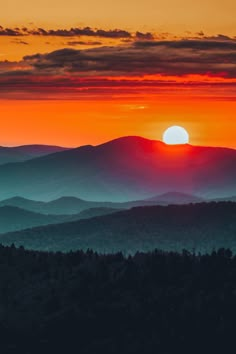 the sun is setting over mountains and trees