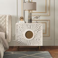 a white nightstand with a lamp on top of it next to a bed and rug