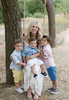 a woman sitting on a swing with two children in front of her and another child standing next to her