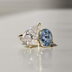 two pear shaped diamond and blue topaz ring on white surface with reflection in background