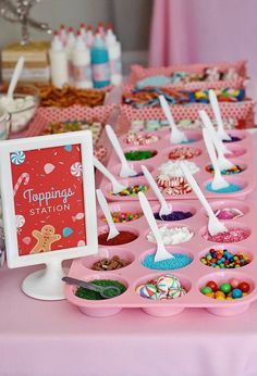 a pink table topped with lots of cupcakes and desserts next to a sign