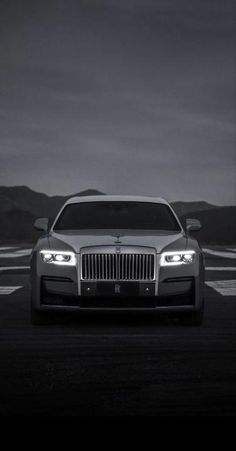 the front end of a silver car on a dark road with mountains in the background