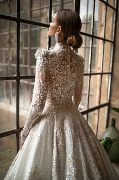 a woman standing in front of a window wearing a dress with long sleeves and an open back