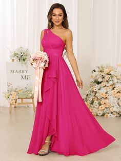 a woman in a long pink dress standing next to a flower arrangement and holding a bouquet