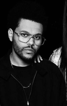 a black and white photo of a man with glasses looking at the camera while standing next to a woman