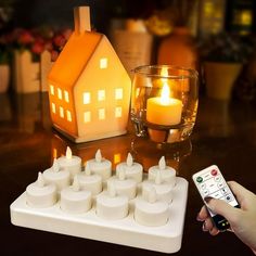 a person holding a remote control next to a lit house and candles on a table