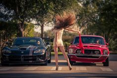 a woman walking across the street next to two cars with her hair blowing in the wind