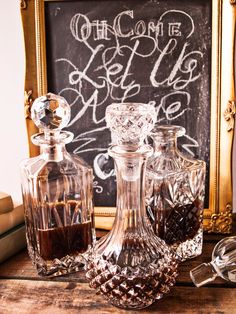 three glass decanters sitting on top of a wooden table next to a chalkboard