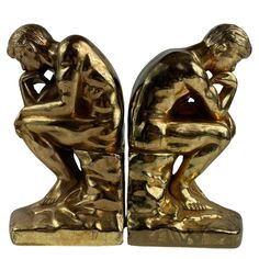 two gold colored figurines sitting next to each other with their hands on their knees