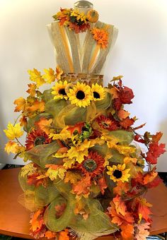 an arrangement of sunflowers and fall leaves is displayed on a table in front of a mannequin