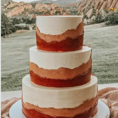 a three tiered cake sitting on top of a table next to a green field