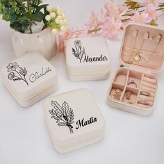 four personalized jewelry boxes with rings and necklaces in them on a table next to flowers