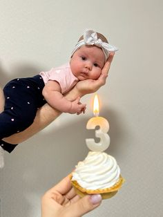 a woman holding a baby next to a birthday cupcake