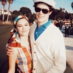 a man and woman standing next to each other in front of palm trees on a sunny day