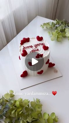 a white cake with red hearts on it sitting on top of a table next to flowers