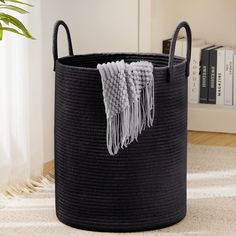 a large black basket with tassels on the handles is sitting in front of a bookshelf