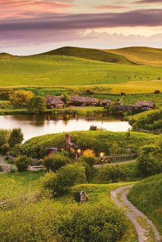 a small lake surrounded by lush green fields and hills with houses on the hill in the distance