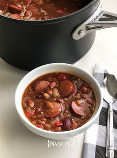 a bowl of beans and sausage stew next to a pot of soup on a table