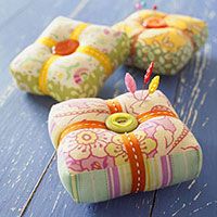 two decorative cushions with buttons on them sitting on a blue table top, one has a pincust in the middle