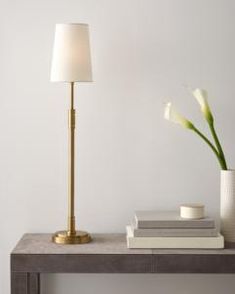 a table with a lamp, vase and books on it next to a white wall