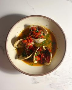 a bowl of soup with clams, tomatoes and parsley in it on a white table