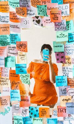 a woman in an orange dress is taking a selfie with her cell phone surrounded by post it notes