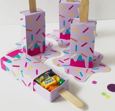 an ice cream box with popsicle sticks and candy in it on a white surface