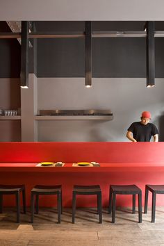 a man standing behind a red counter in a restaurant with four stools next to it