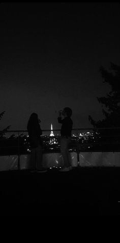 two people standing next to each other in front of the eiffel tower at night