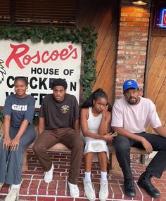 four people sitting on a bench in front of a house of chicken n'fish