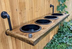 three black bowls sitting on top of a wooden shelf in front of a wood fence