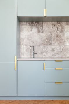 a kitchen with blue cabinets and gold pulls on the handles, marble counter tops, and wooden flooring