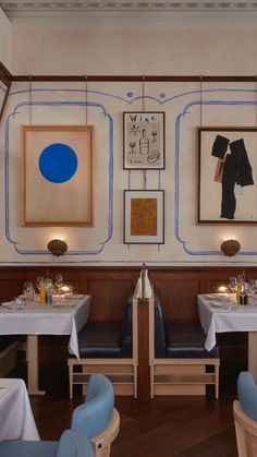 a restaurant with blue chairs and white tablecloths on the tables, framed pictures above them