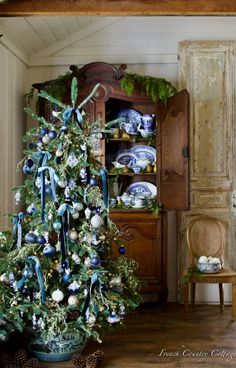 a christmas tree with blue and white ornaments in a potted planter next to a china cabinet