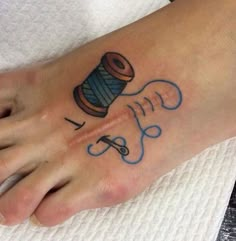 a person with a tattoo on their foot has a spool of thread and scissors